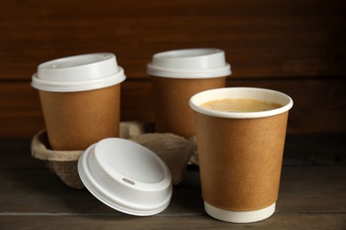 Takeaway paper coffee cups with plastic lids and cardboard holder on wooden table