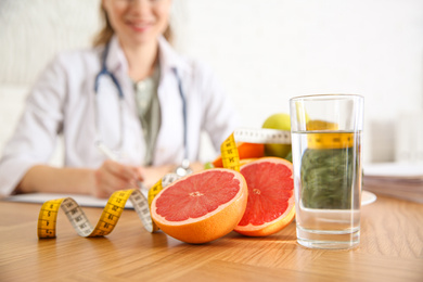 Photo of Glass of water, grapefruit, measuring tape and blurred nutritionist on background