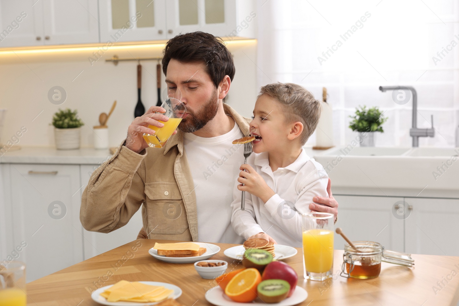 Photo of Father and his cute little son having breakfast at table in kitchen