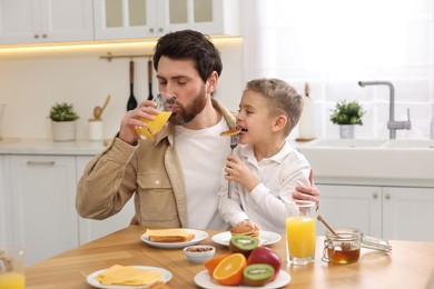 Photo of Father and his cute little son having breakfast at table in kitchen