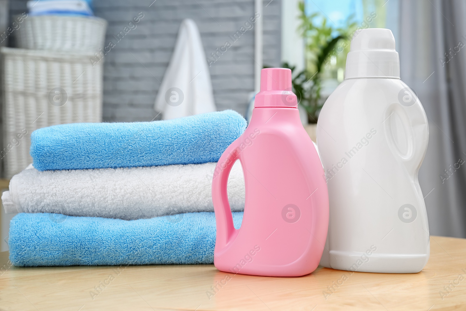 Photo of Stack of clean towels and bottles with detergent on table