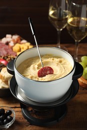 Photo of Fork with piece of sausage and melted cheese in fondue pot on wooden table