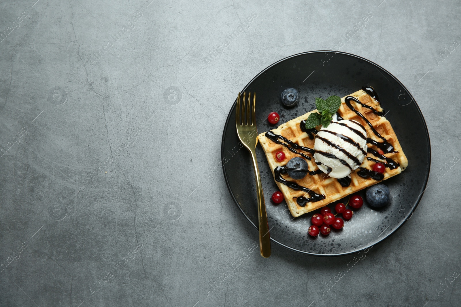Photo of Delicious Belgian waffle with ice cream, berries and chocolate sauce on grey textured table, top view. Space for text