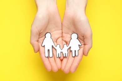 Woman holding paper family cutout on yellow  background, top view