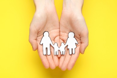 Photo of Woman holding paper family cutout on yellow  background, top view