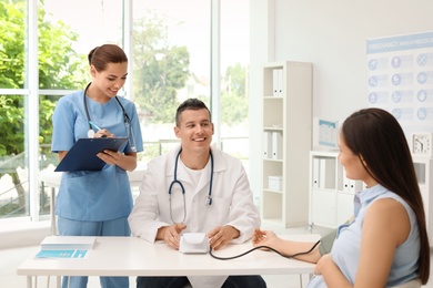 Photo of Doctor and his assistant checking pregnant woman's blood pressure in hospital. Patient consultation