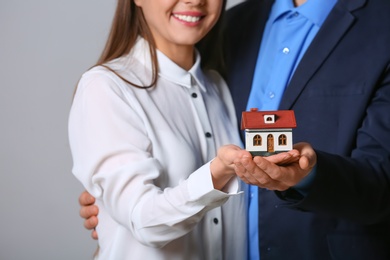Young couple holding house model on grey background, closeup. Home insurance