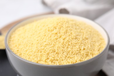 Photo of Raw couscous in bowl on table, closeup