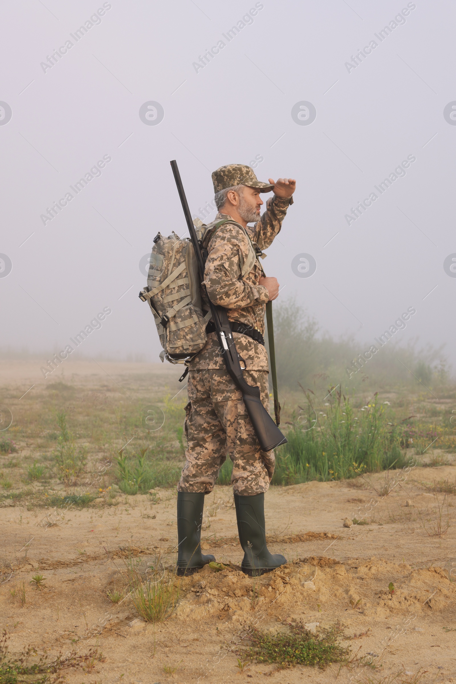 Photo of Man wearing camouflage with hunting rifle and backpack outdoors