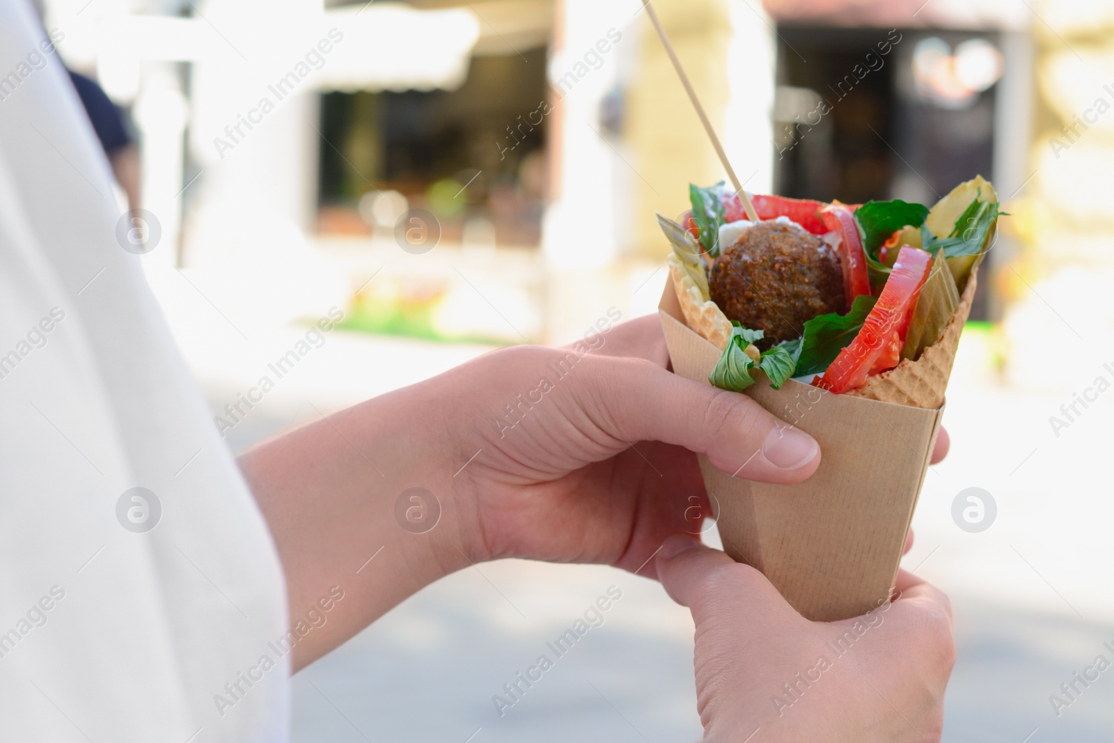 Photo of Woman holding wafer with falafel and vegetables outdoors, closeup. Street food