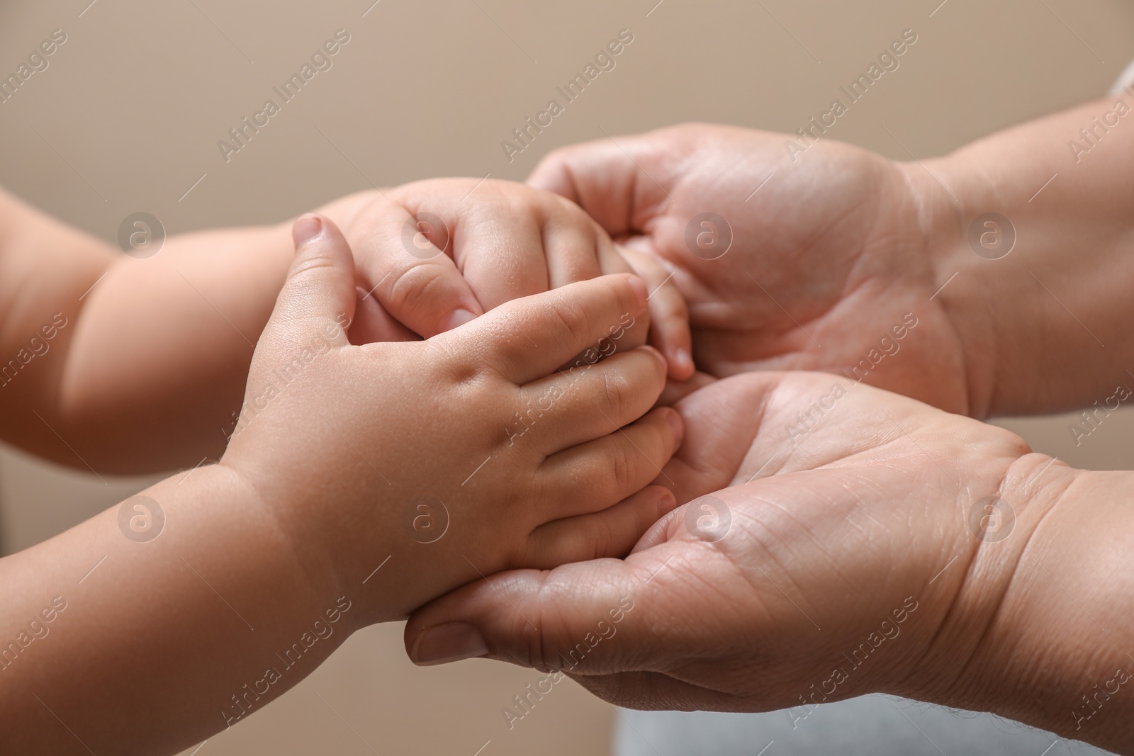 Photo of Woman holding hands with her granddaughter on beige background, closeup