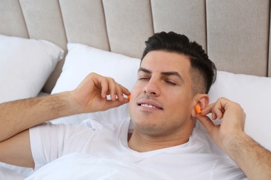 Photo of Man inserting foam ear plugs in bed