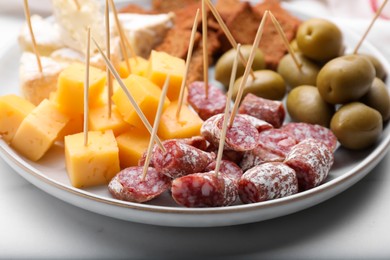 Photo of Toothpick appetizers. Pieces of sausage and cheese on white table, closeup