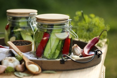 Jars of delicious pickled cucumbers and ingredients on wooden table against blurred background, closeup