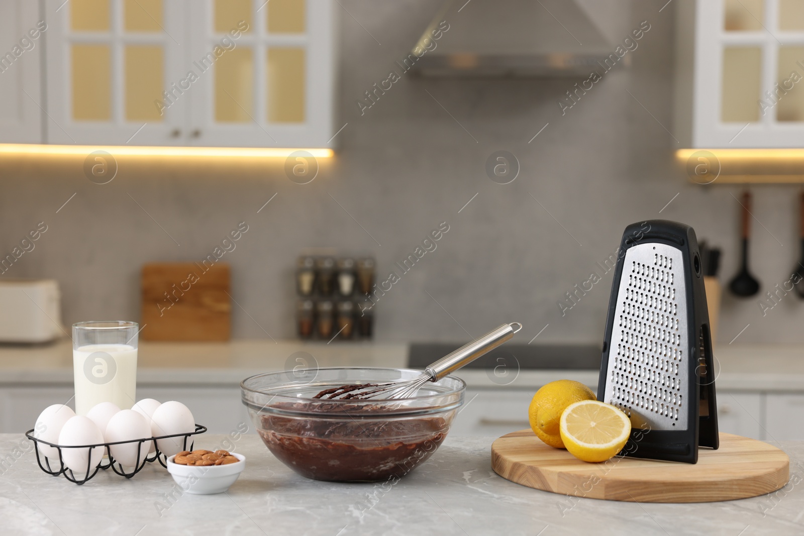 Photo of Metal whisk, chocolate cream in bowl, grater and different products on gray marble table indoors