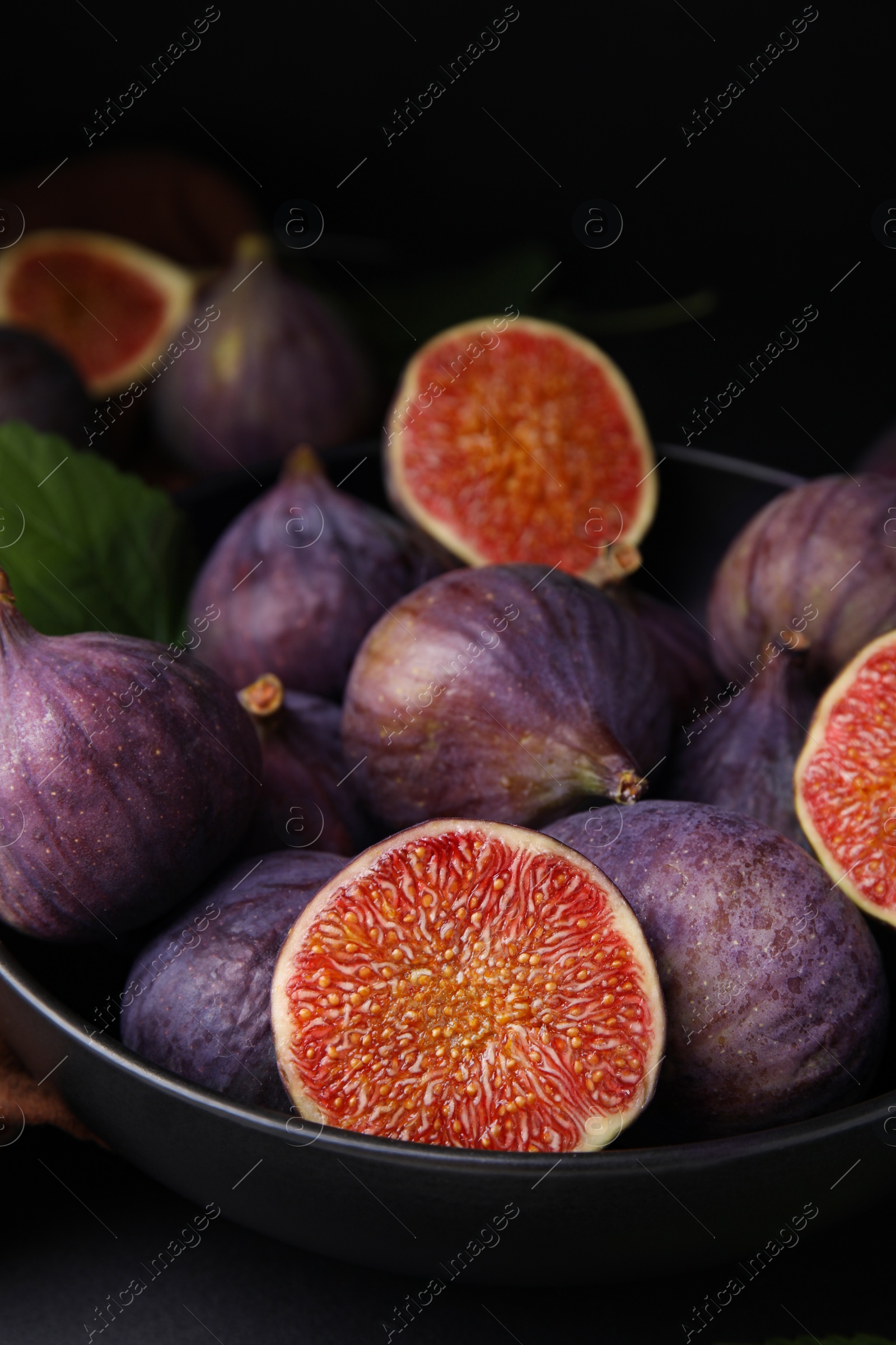 Photo of Bowl with fresh ripe purple figs on black table, closeup