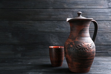 Brown clay jug and cup on black wooden table, space for text. Handmade utensils