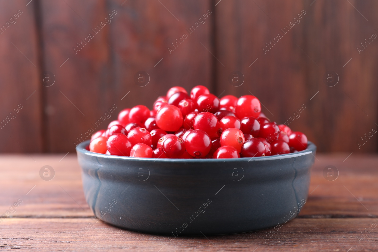 Photo of Fresh ripe cranberries in bowl on wooden table, closeup