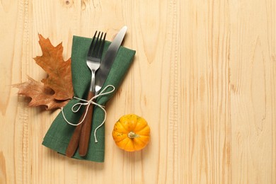 Photo of Napkin, cutlery and pumpkin on light wooden background, flat lay with space for text. Stylish autumn table setting