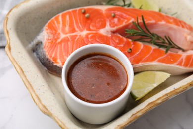 Fresh marinade, fish, lime and rosemary in baking dish on light table, closeup