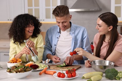 Photo of Friends cooking healthy vegetarian meal at white marble table in kitchen