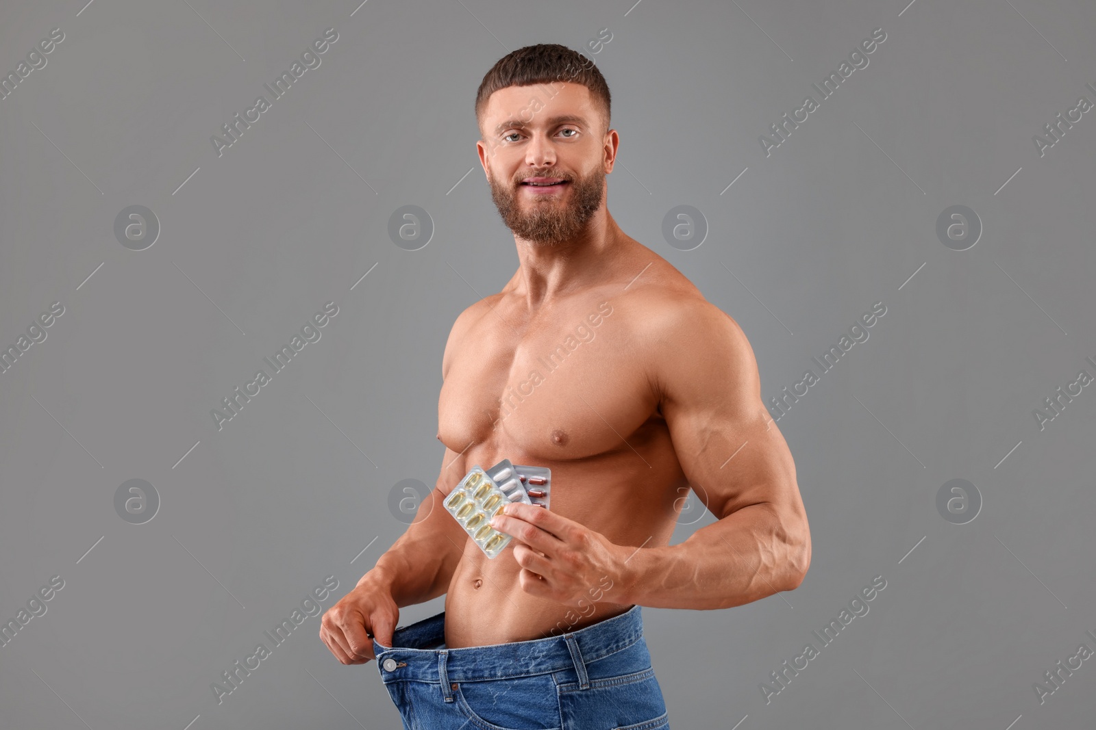 Photo of Athletic young man with pills wearing big jeans on grey background. Weight loss