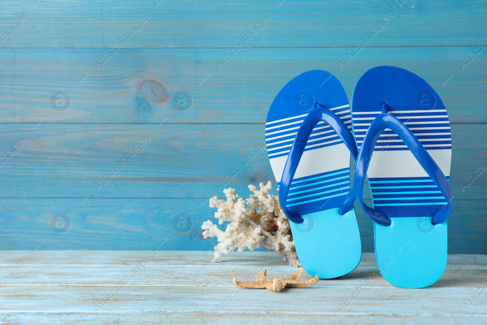 Photo of Stylish flip flops, coral and starfish near light blue wooden wall, space for text