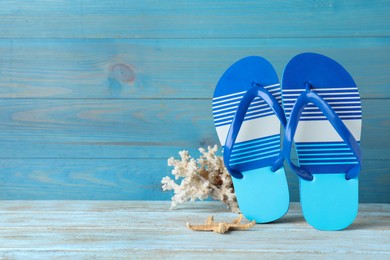 Stylish flip flops, coral and starfish near light blue wooden wall, space for text