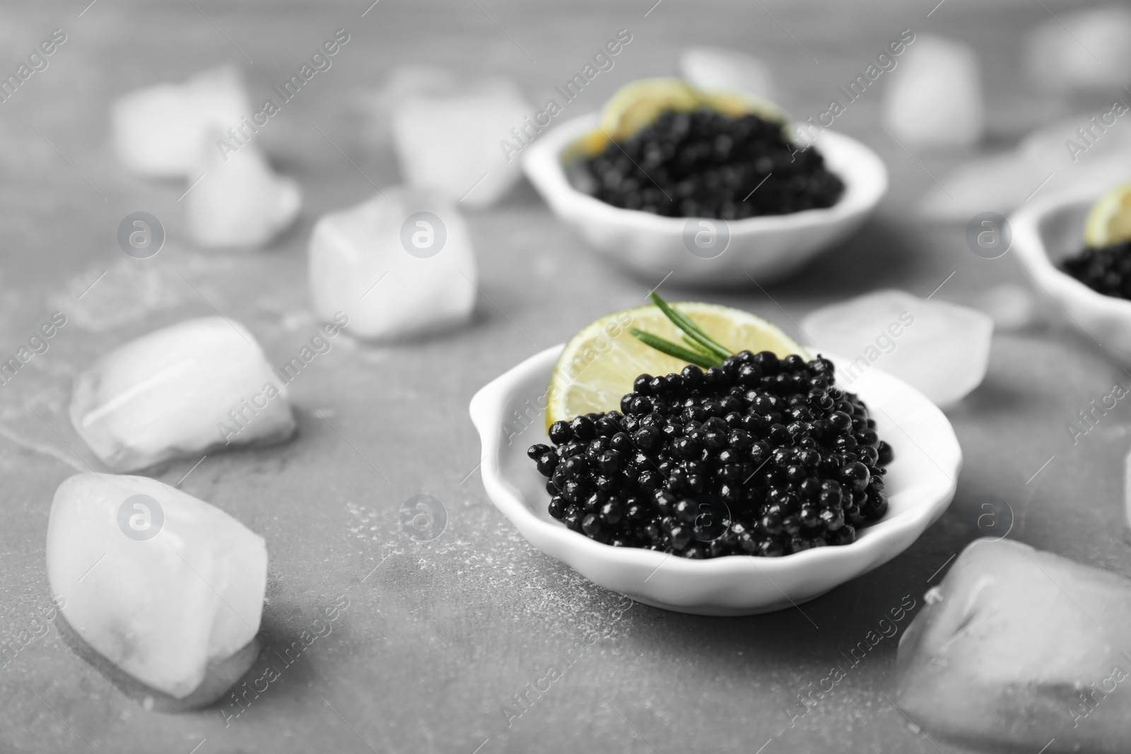 Photo of Plate with black caviar and ice cubes on grey background
