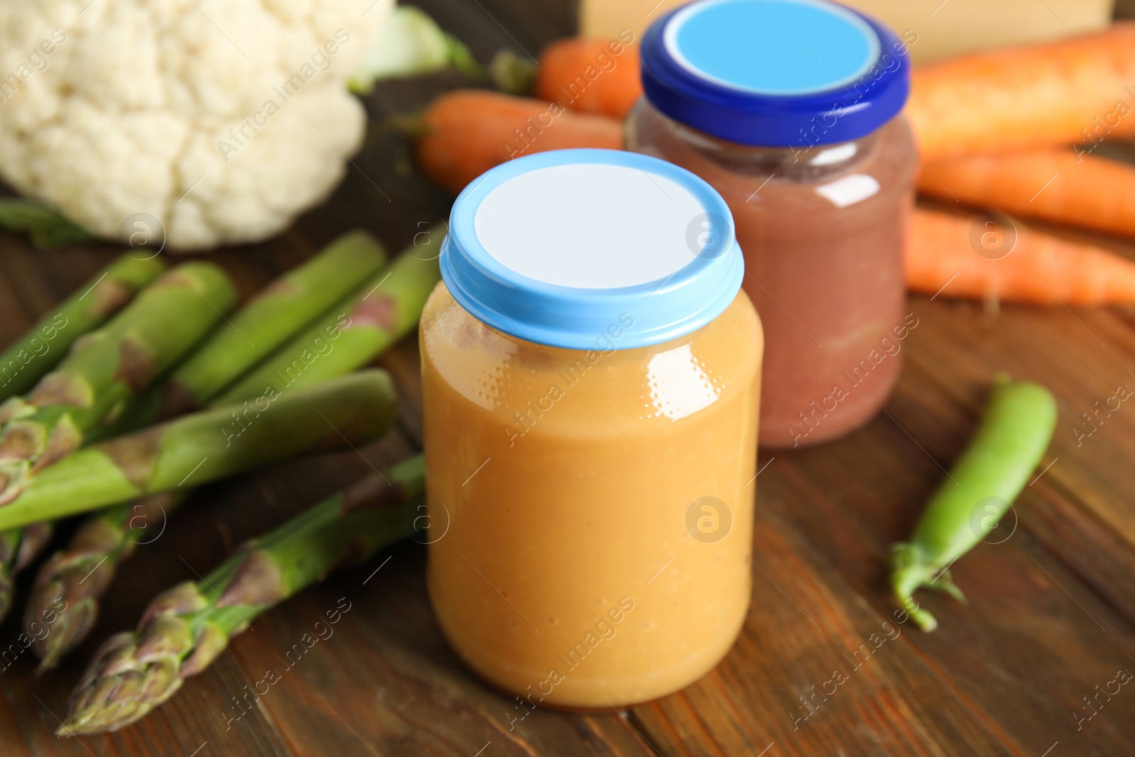 Photo of Jars with baby food and fresh vegetables on wooden table