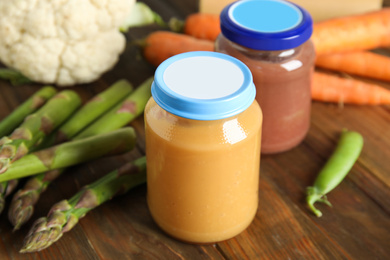 Photo of Jars with baby food and fresh vegetables on wooden table