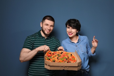 Attractive young couple with delicious pizza on color background