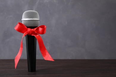 Photo of Microphone with red bow on wooden table against grey background, space for text. Christmas music