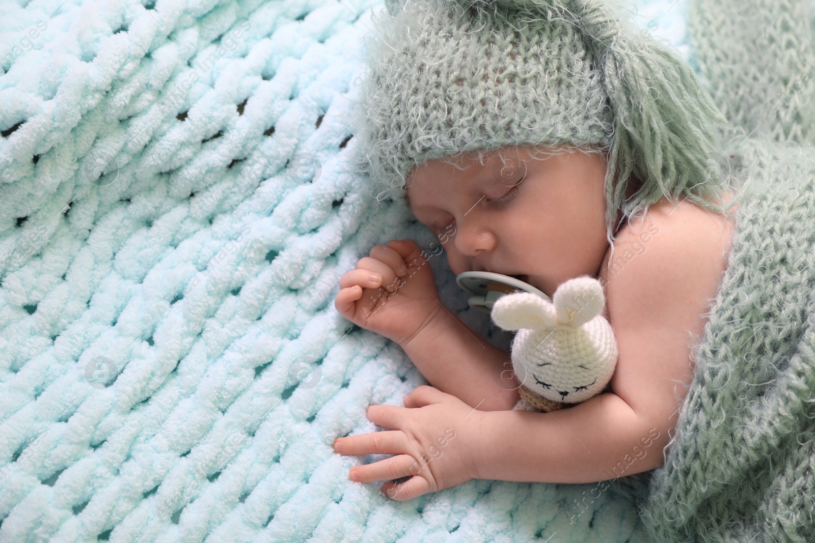 Photo of Cute newborn baby with pacifier sleeping on light blue blanket, top view. Space for text