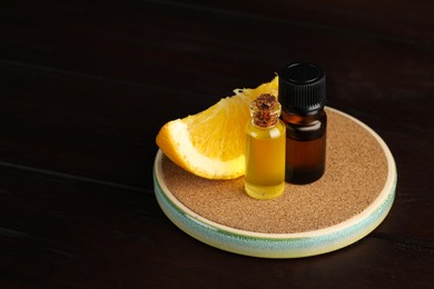 Photo of Bottles of essential oil and orange on wooden table, space for text