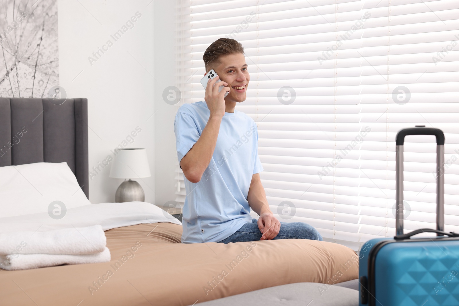 Photo of Smiling guest talking by smartphone on bed in stylish hotel room