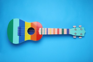 Photo of Colorful ukulele on light blue background, top view. String musical instrument