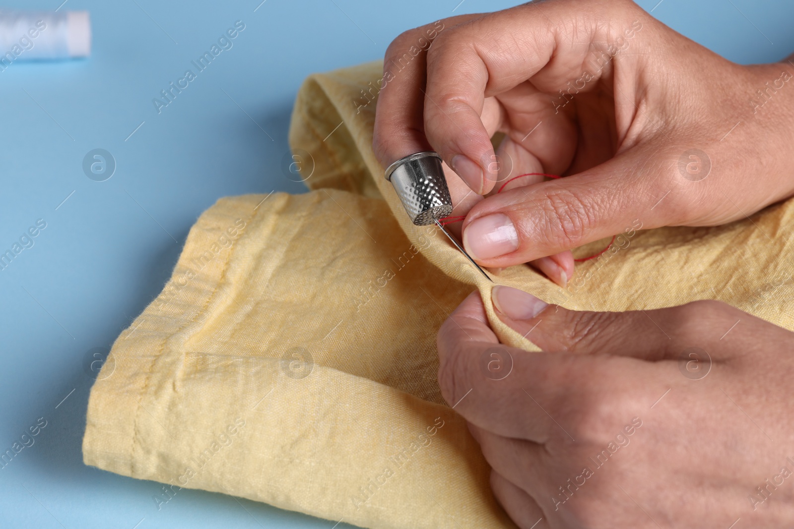 Photo of Woman sewing with thimble and needle on light blue background, closeup