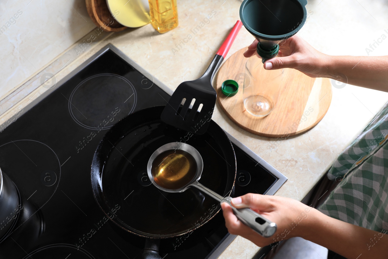 Photo of Woman with used cooking oil, empty bottle and funnel near stove in kitchen, closeup