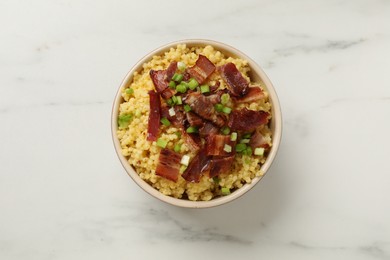 Tasty millet porridge with bacon and green onion in bowl on white marble table, top view