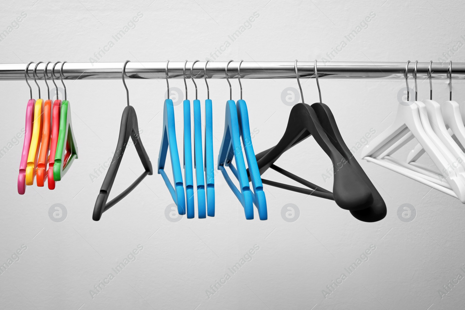 Photo of Clothes hangers on metal rail against light background