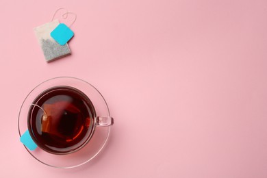 Photo of Tea bags and cup of hot drink on pink background, flat lay. Space for text