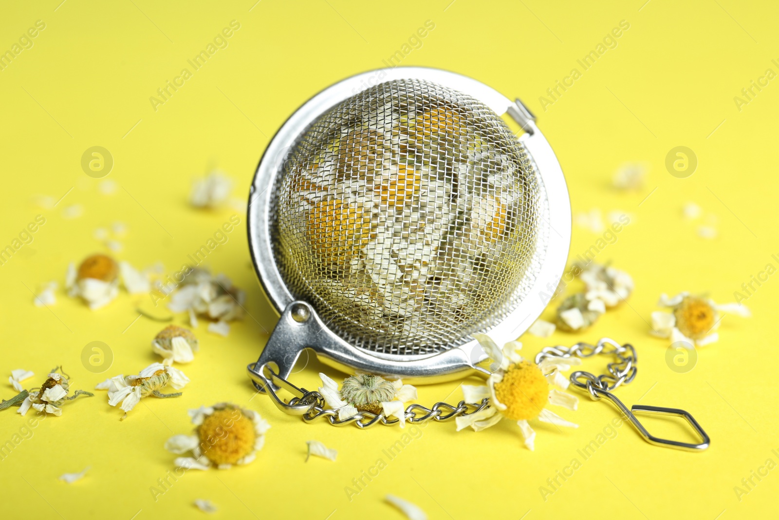 Photo of Dry chamomile flowers in infuser on yellow background, closeup