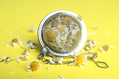 Photo of Dry chamomile flowers in infuser on yellow background, closeup