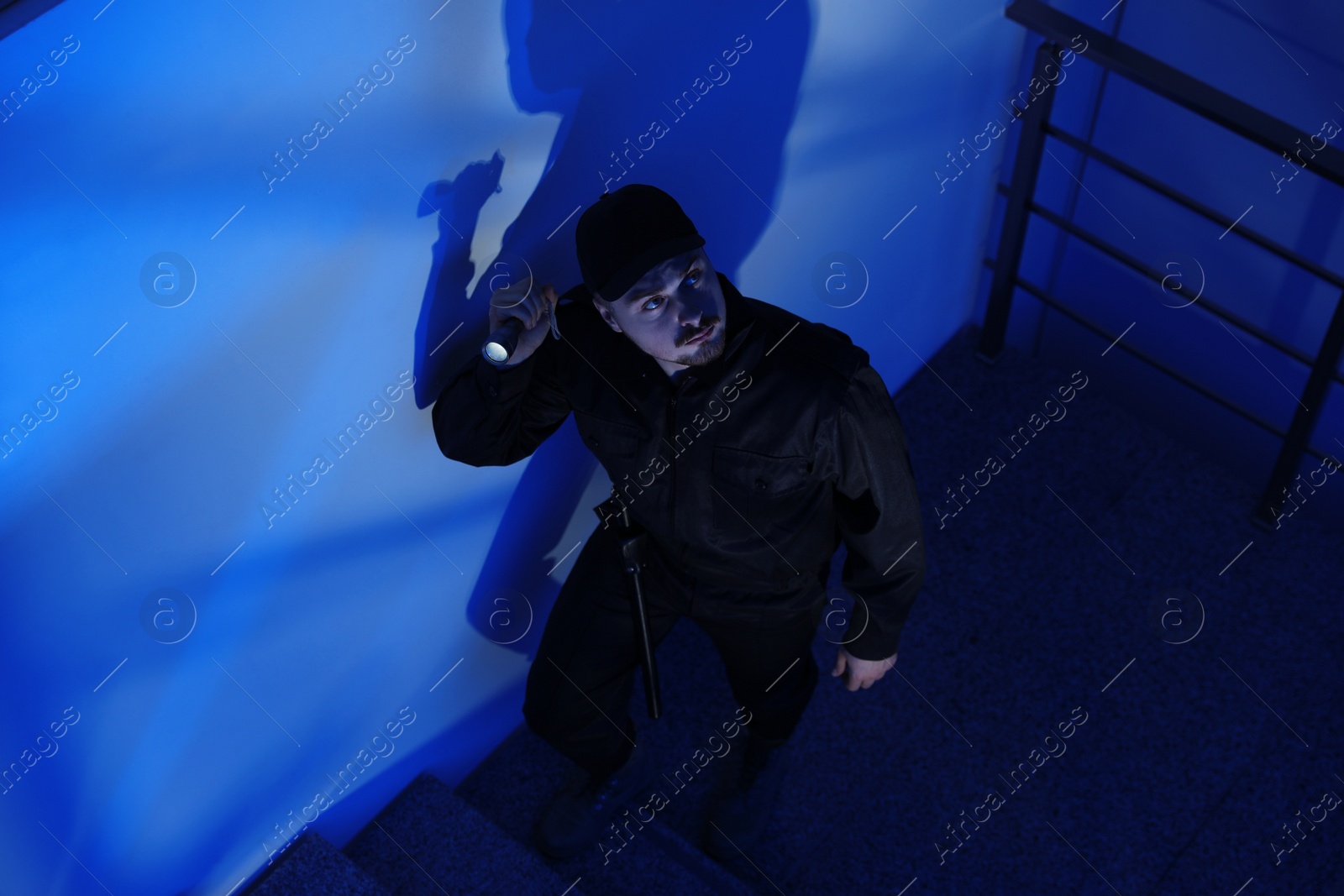 Photo of Male security guard with flashlight going up stairs in darkness