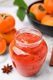 Photo of Jar of tasty persimmon jam and ingredients on white marble table, above view