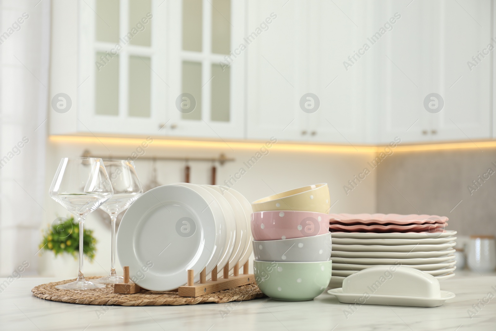 Photo of Clean plates, bowls, butter dish and glasses on white marble table in kitchen