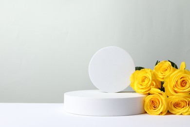 Photo of Beautiful presentation for product. Geometric figures and yellow roses on white table against light grey background, space for text