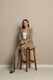 Photo of Beautiful young businesswoman sitting on stool near beige wall