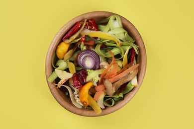 Photo of Peels of fresh vegetables in bowl on yellow background, top view